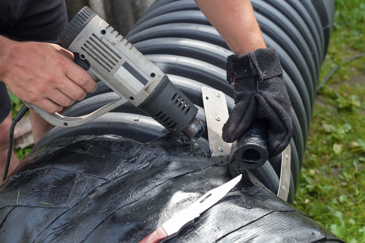 a man attaching a roofing material around a large pipe