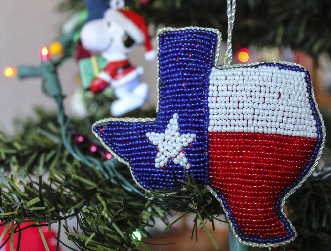 red, white, and blue beaded Texas ornament on lighted artificial Christmas tree with Peanuts character Snoopy ornament in background