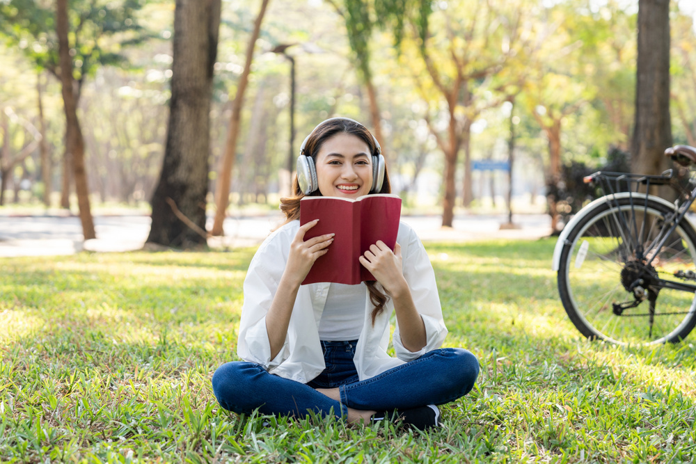 Young asian woman relaxing reading book sitting at public park life style outdoor. Happy female Take a break enjoy time living in the nature. Human and nature together