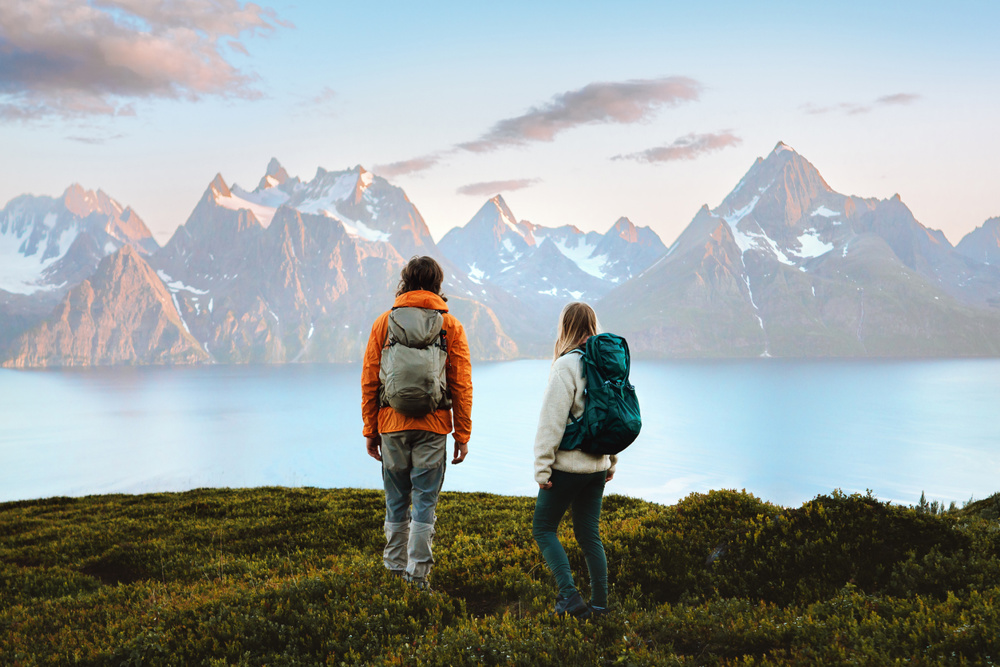 Couple enjoying mountains landscape in Norway friends man and woman hiking with backpack, active vacations healthy lifestyle outdoor family adventurers exploring trails in Lyngen Alps survival trip