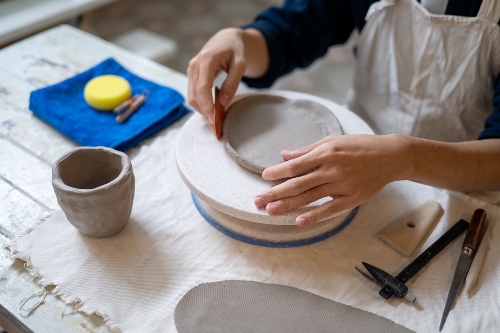 Close up of potter artist scraping on clay to make a plate on working table in pottery class or studio. Ceramic making, Handmade Product, Art Workshop