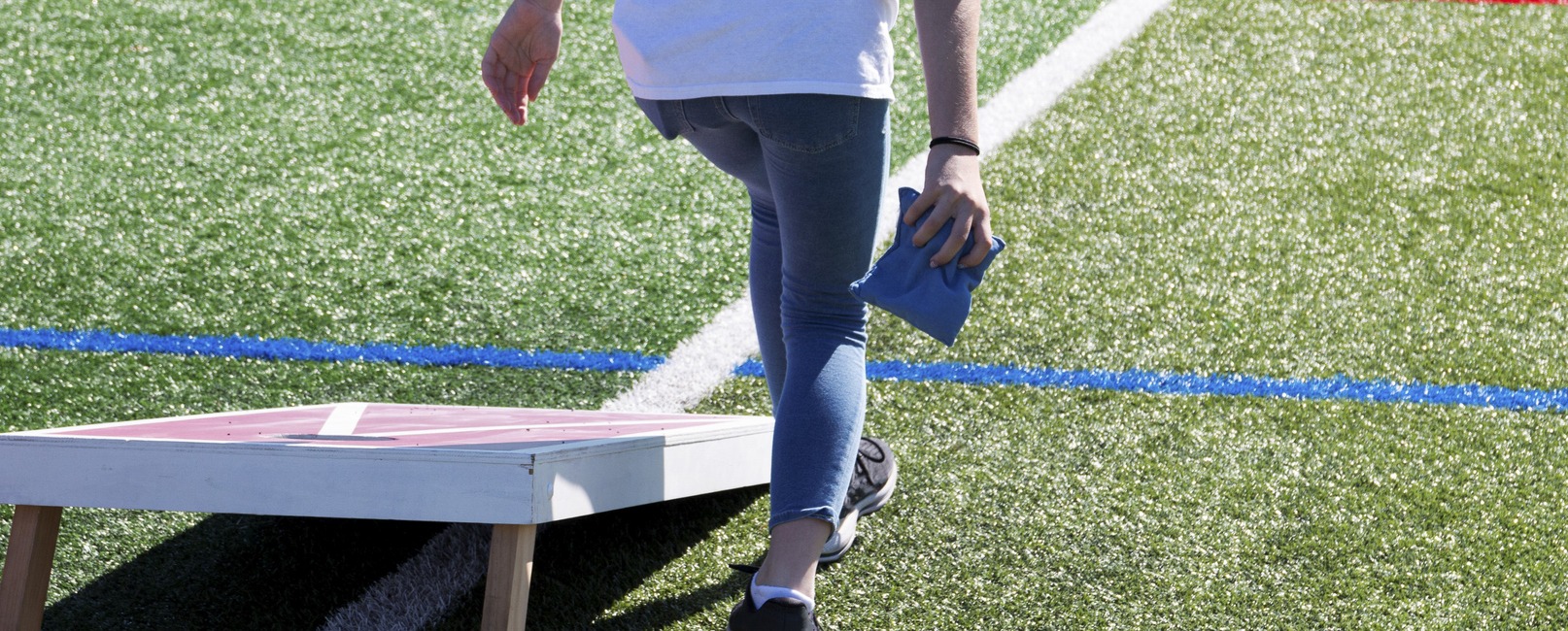 Person throwing a blue bean bag playing cornhole