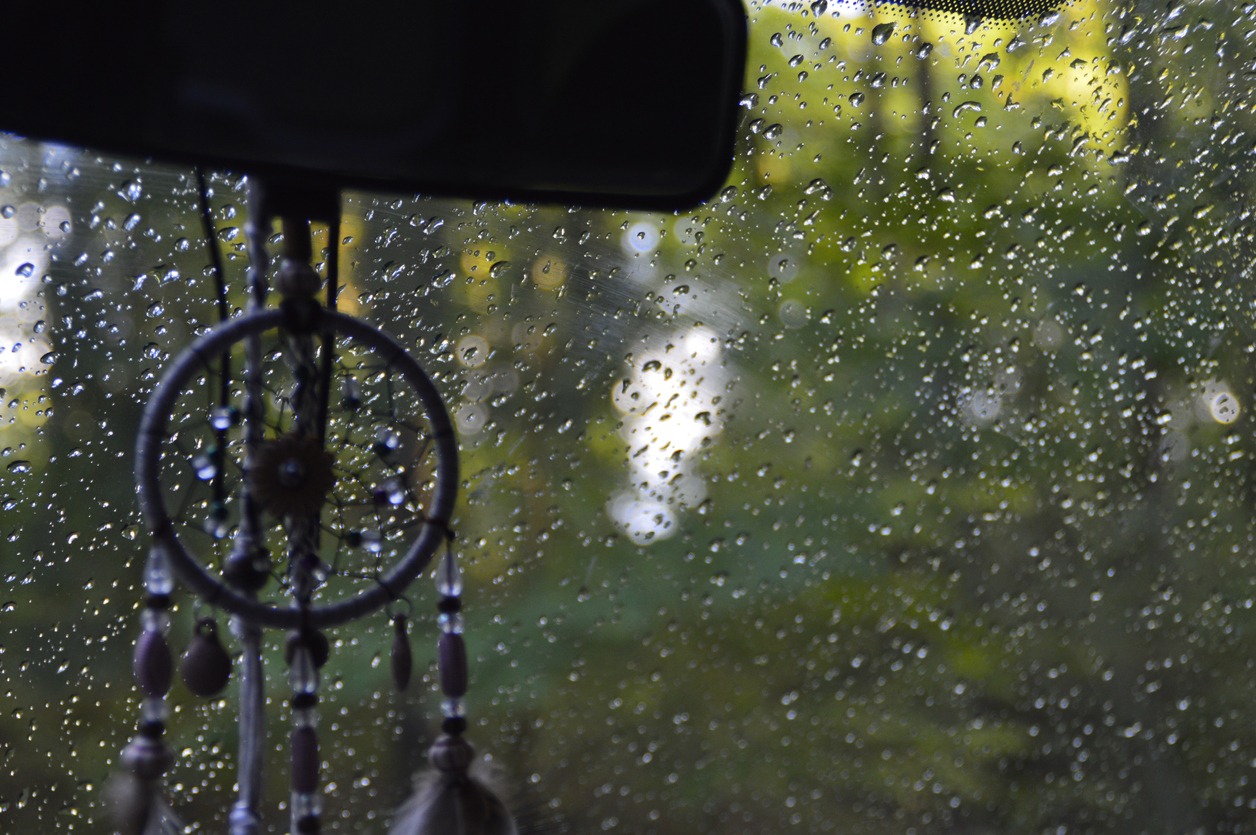 Dreamcatcher hanging from a car mirror with rain in the background