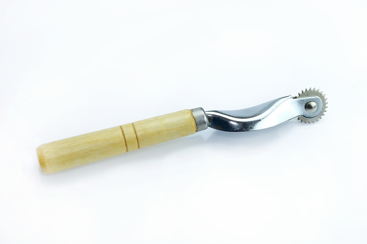 Metallic tracing wheel with wooden handle on white background.