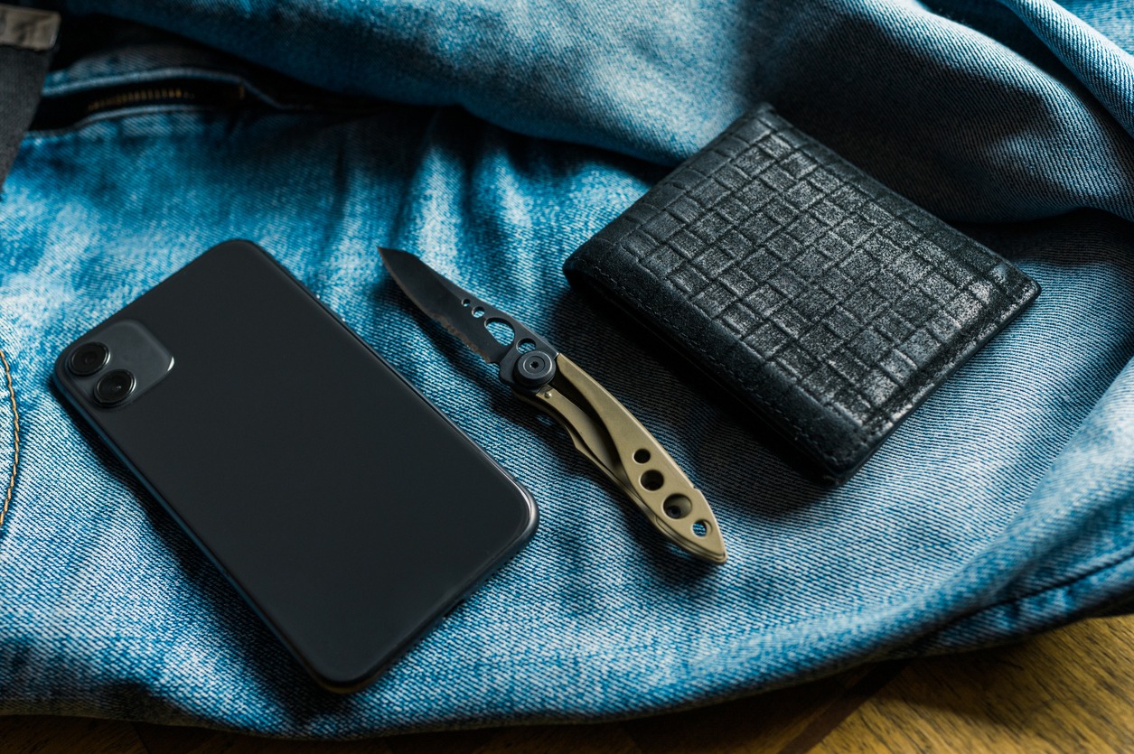 EDC concept on men's jeans. Everyday carry a pocket dump of multitool, wallet, flashlight, folding knife, lighter, paracord bracelet, and tourniquet