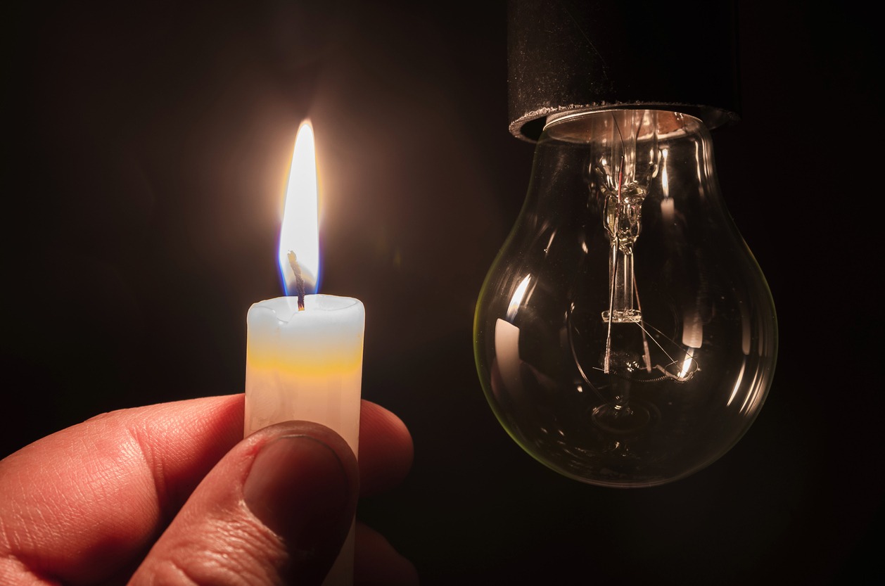 Burning candle near a switched off light bulb in complete darkness