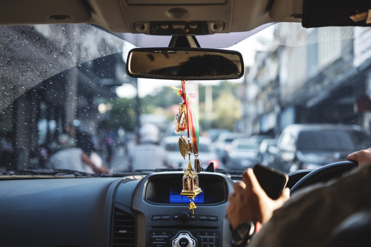 Amulets hanging from the car mirror in a car driving down a road