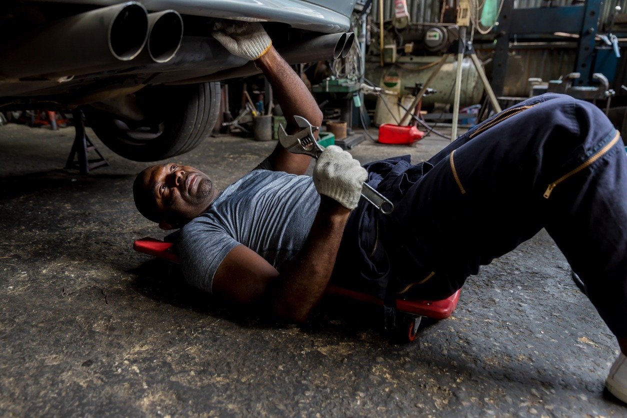Mechanic lying down and working under car at auto service garage. Technician vehicle maintenance and checking under car at automotive motor garage