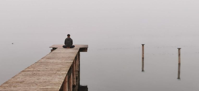 Image of a man meditating on a wooden body built on a lake.