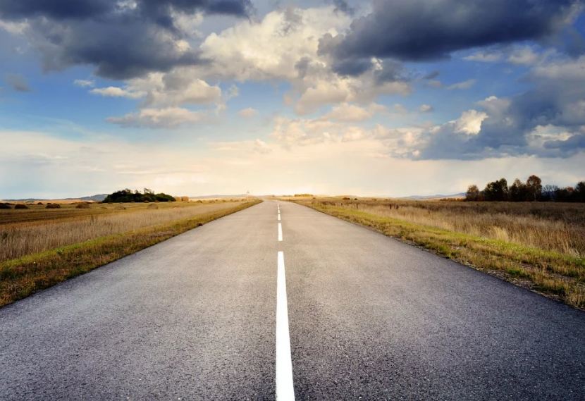 Image of an empty road with a clear sunny sky.