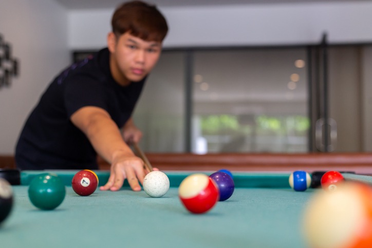 A man in black shirt playing pool or billiard in a pool hall, focus on background, horizontal