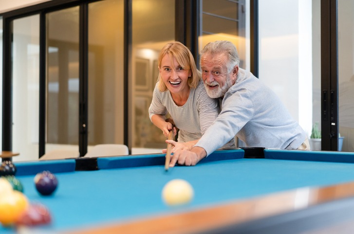Lovers in a living room. Happy senior couple playing billiards together in home.