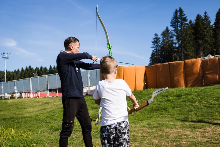 Father and son practicing archery outdoors.