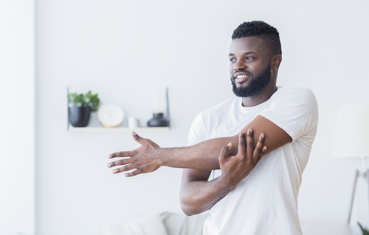 Young black man training and stretching arm at home