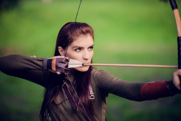 Art photo of a young woman with arrows and a bow on a green meadow background