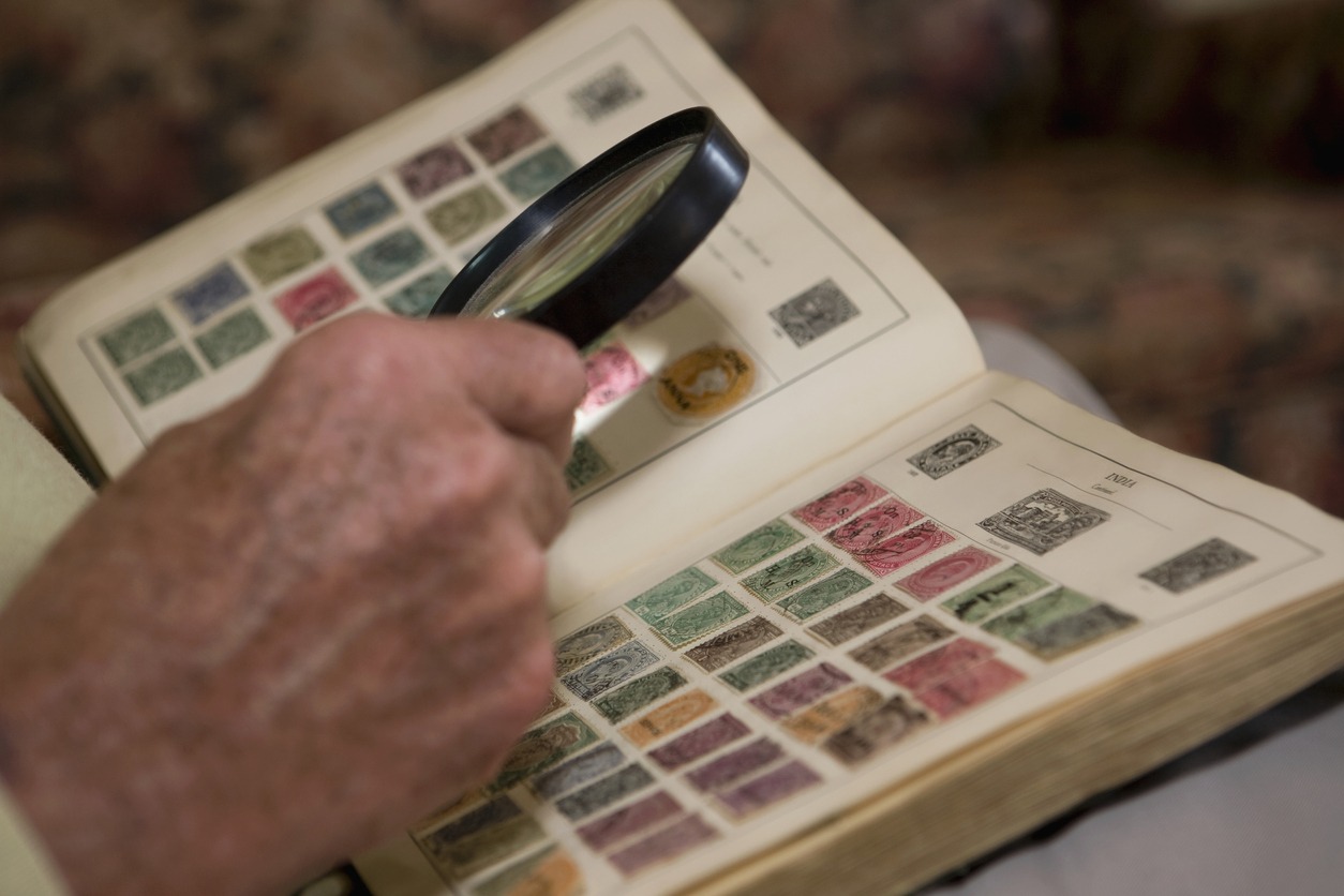 Man's Hand Examining An Old Stamp Book With Magnifying Glass