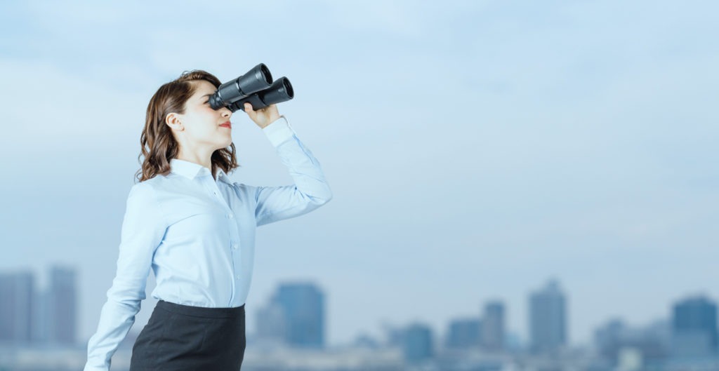 Young businesswoman using binoculars in front of the city