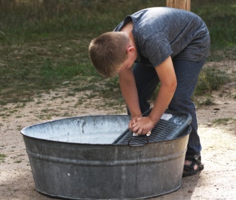 A-boy-washing-clothes-in-a-metal-tub-using-a-washboard