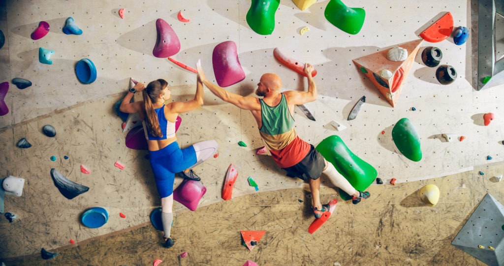 A couple rock climbing on a bouldering wall in a gym