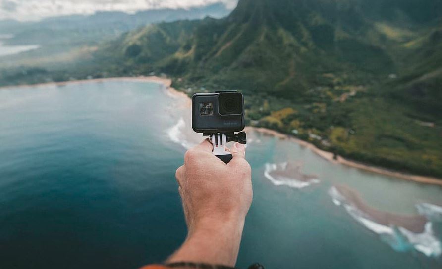 A person using a Go Pro camera to capture a beach landscape