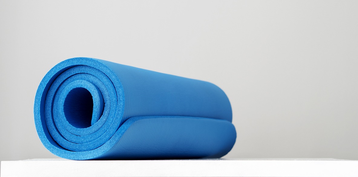 Fitness mat in blue, coiled up, against a gray background.