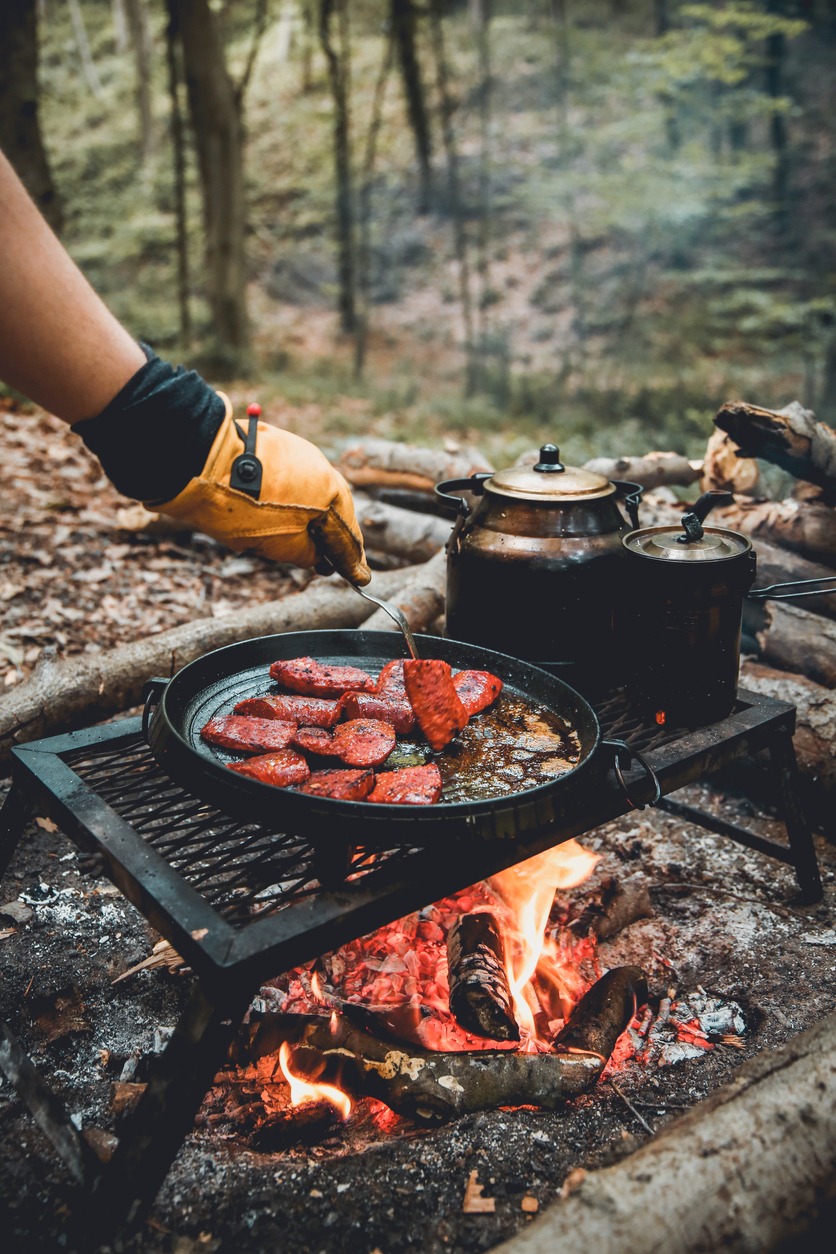 Man cooking food over an open fire in a camping site.