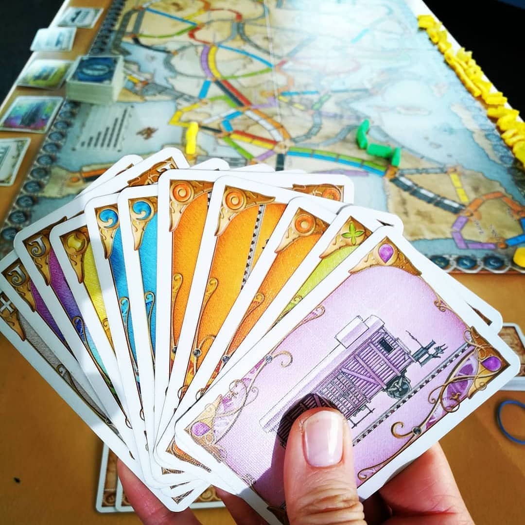 Ticket to Ride cards in hand with the board game being played at the background