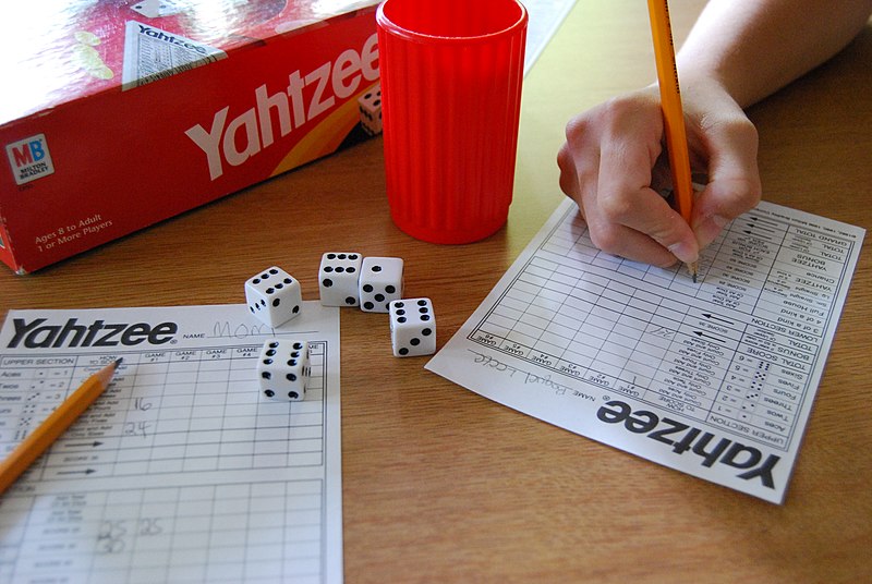 a Yahtzee set on the table with one person writing on the scoresheet
