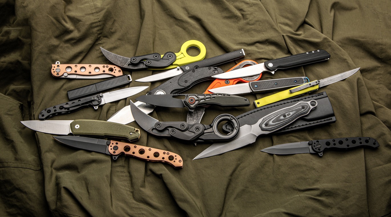A variety of folding and pocket knives lie on khaki fabric. A versatile pocket tool and self-defense tool