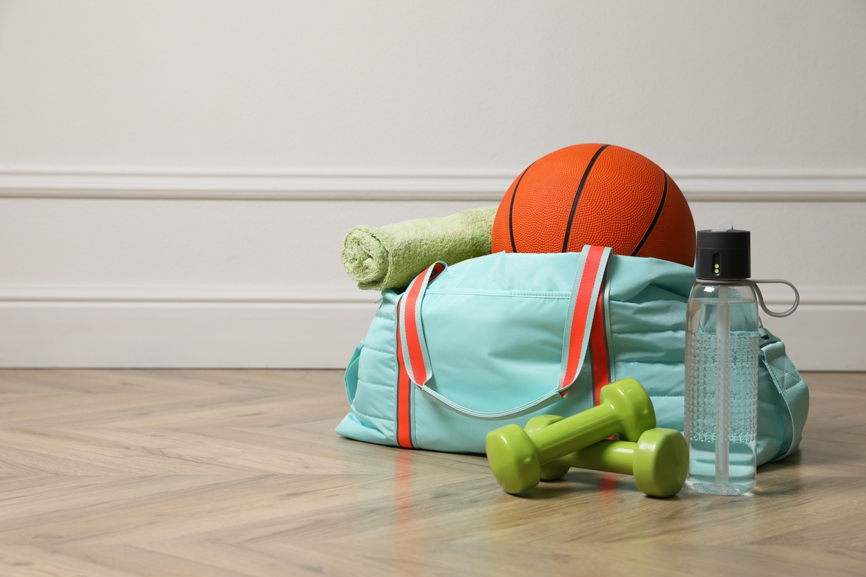 Blue gym bag with sports accessories on floor near white wall indoors, space for text