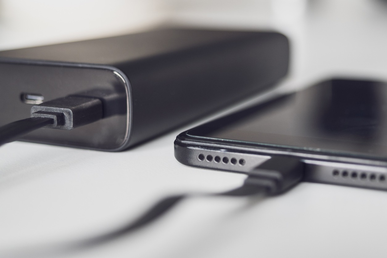 Connecting your phone to a portable charger, close-up. The Power bank and the smartphone are connected by a cable and lie on a white table. Black powerbank and phone on white background