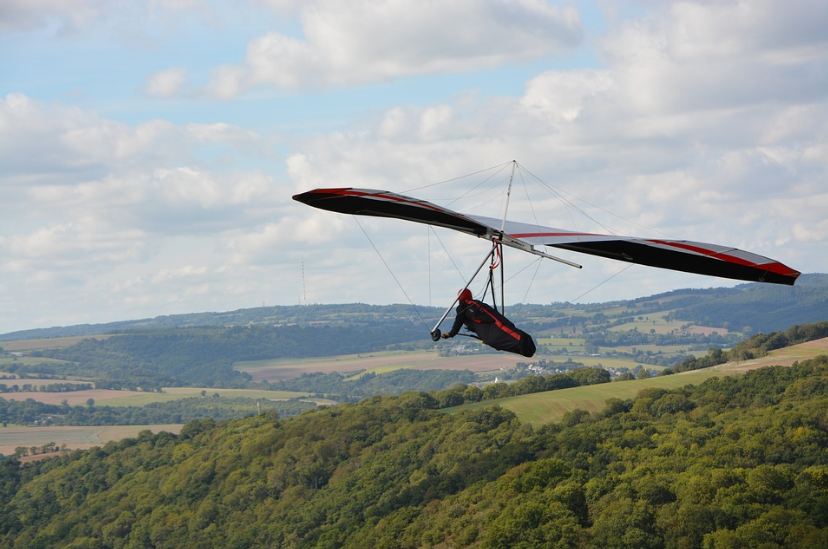 glider-in-a-black-and-red-gear-green-trees-and-mountains-cloudy-sky