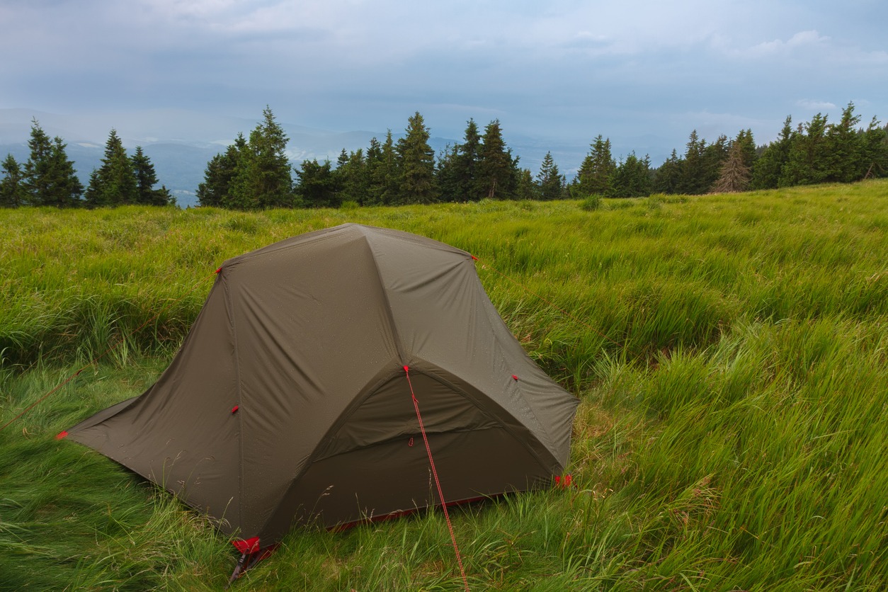 Green lightweight freestanding three-season 2-person tent on mravenecnik hill in grass in the morning after rainstorm
