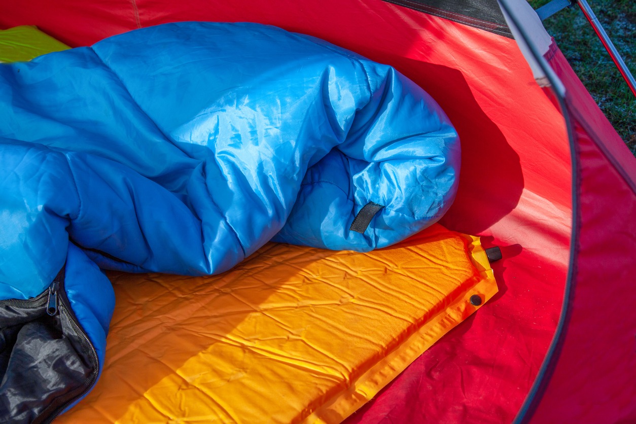 The inside of a red tent with an blue sleeping bag and an orange self-inflating blow-up mattress pad
