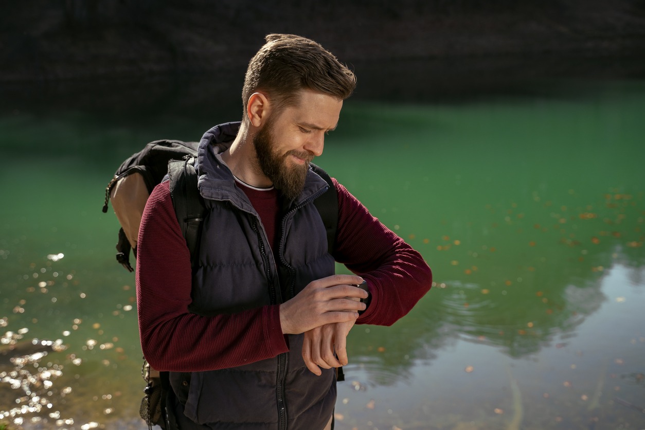 Man with backpack in nature checking parameters on smart watch
