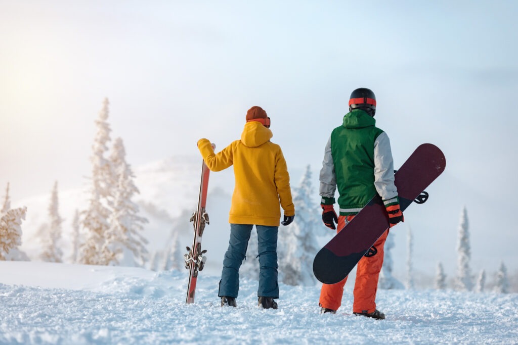 Skier and snowboarder are standing on background of ski resort