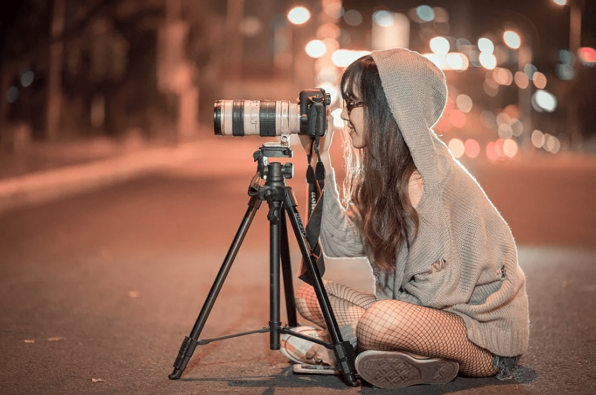 woman-sitting-on-the-ground-tripod-camera-blurred-lights
