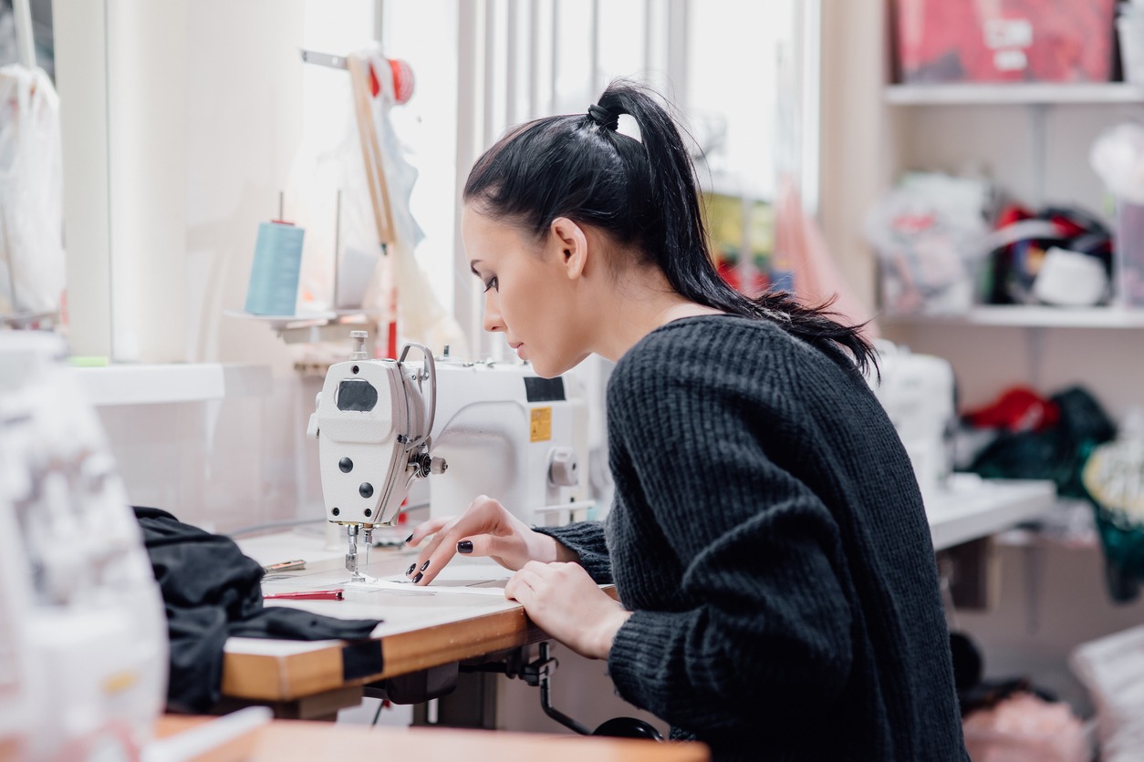 young woman sewing with professional machine at workshop. professional seamstress, authentic image. clothing designer next to the sewing machine,