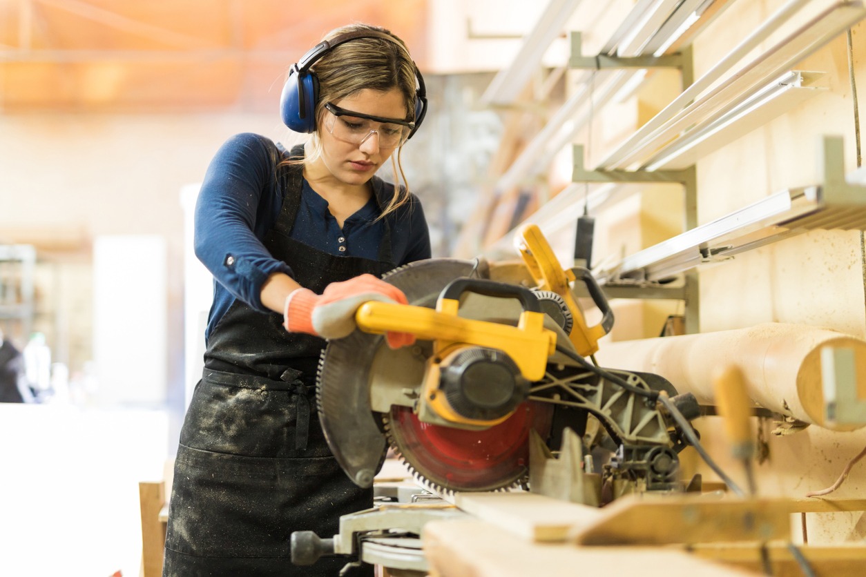 Woman wearing protective gear while using a chop saw