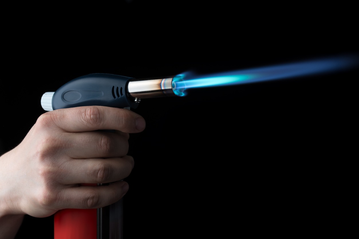 hand holding a butane torch with a blue flame
