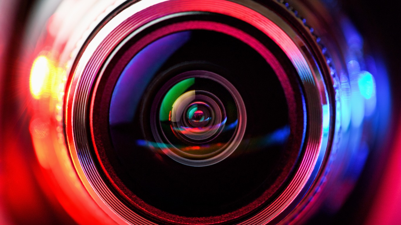 A close up of a camera lens that is being illuminated by different colored lights from every side.