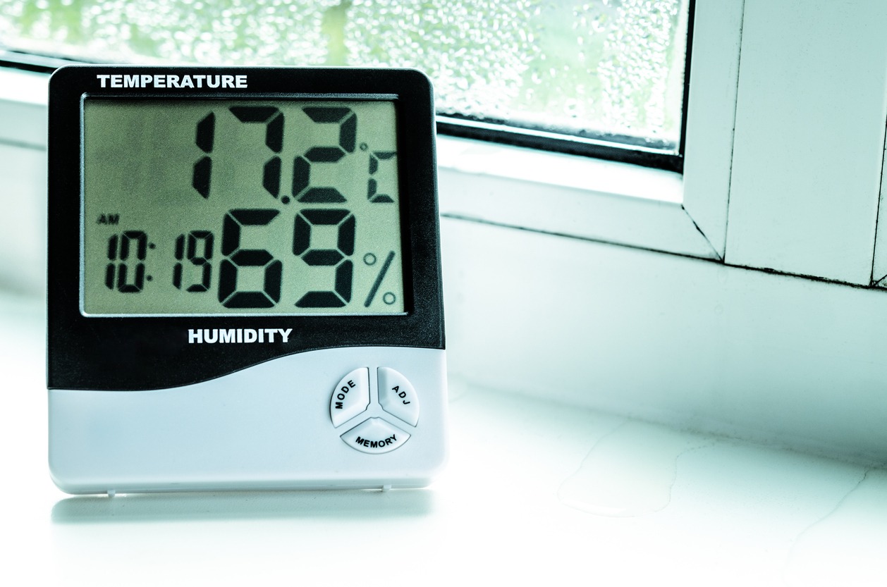 A digital hygrometer placed near a window sill to measure temperature and humidity.