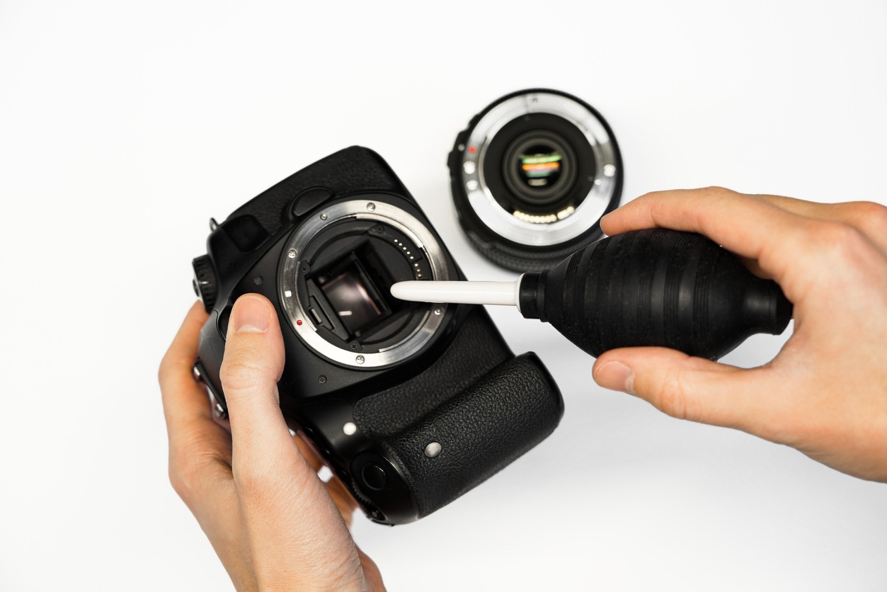 A man using a lens puffer to clean a DSLR camera