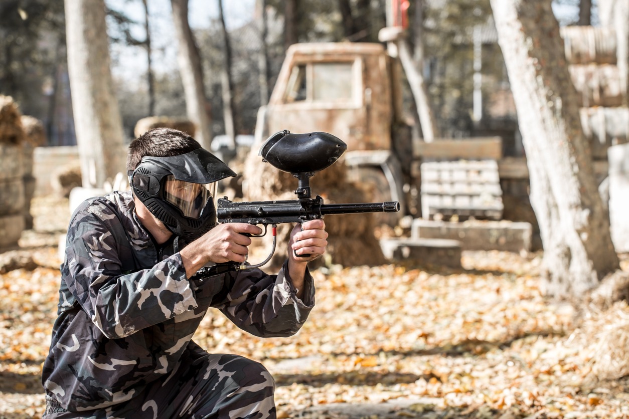 A man with a gun in a uniform and a mask on his face, playing paintball. Sports active games in the fresh air