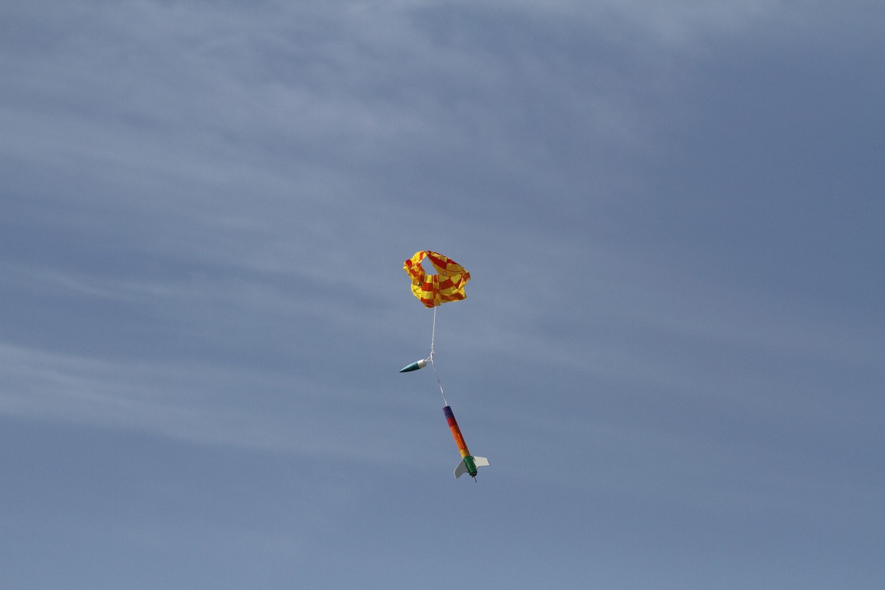A red and yellow parachute attached to a model rocket in the air
