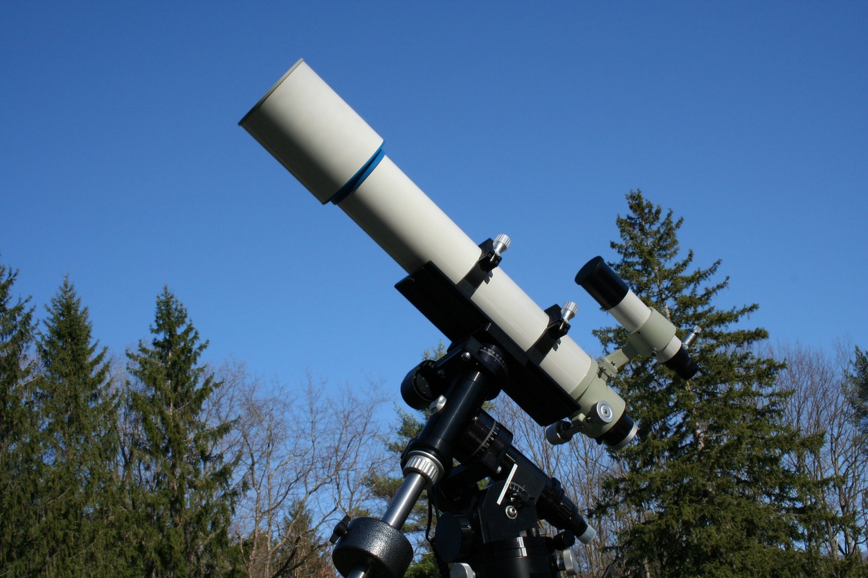 A refractor telescope set up in a field during the day.