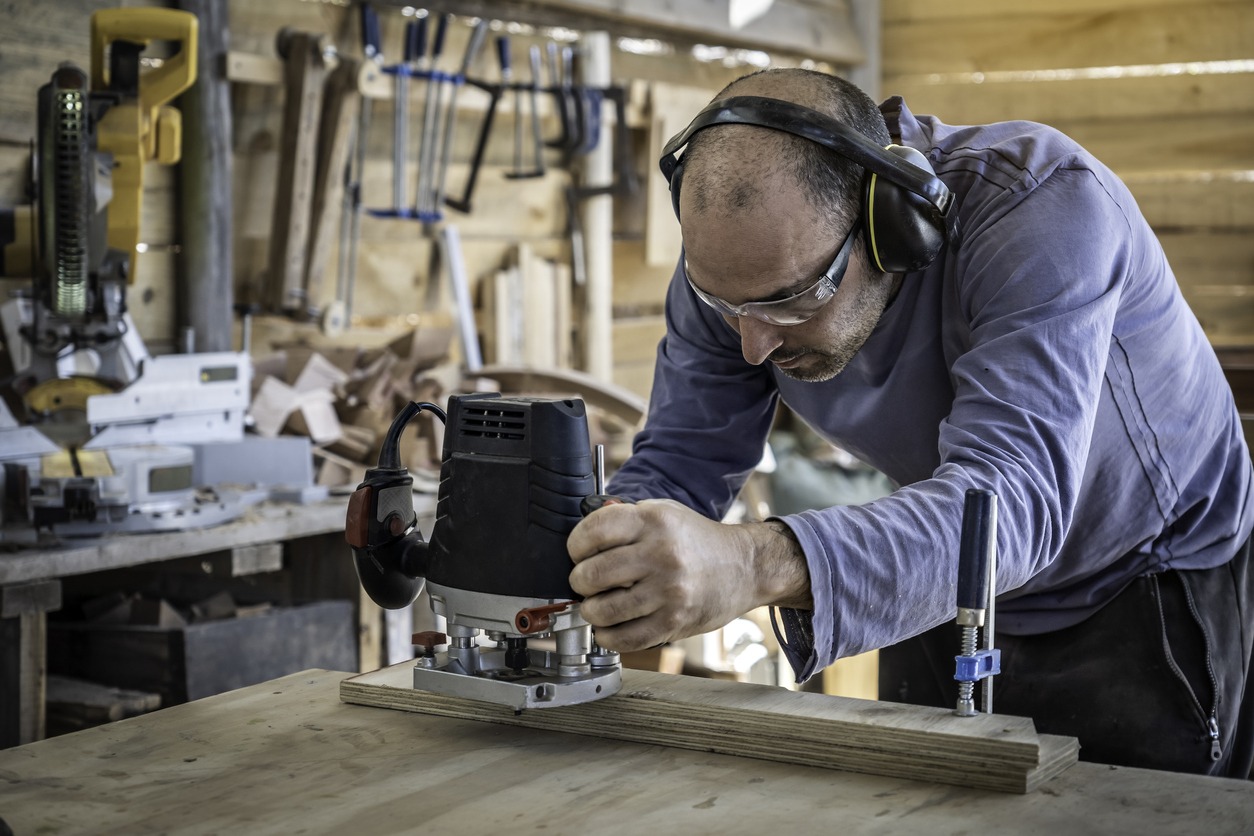 Carpenter making a piece of furniture and using a router at his wood workshop