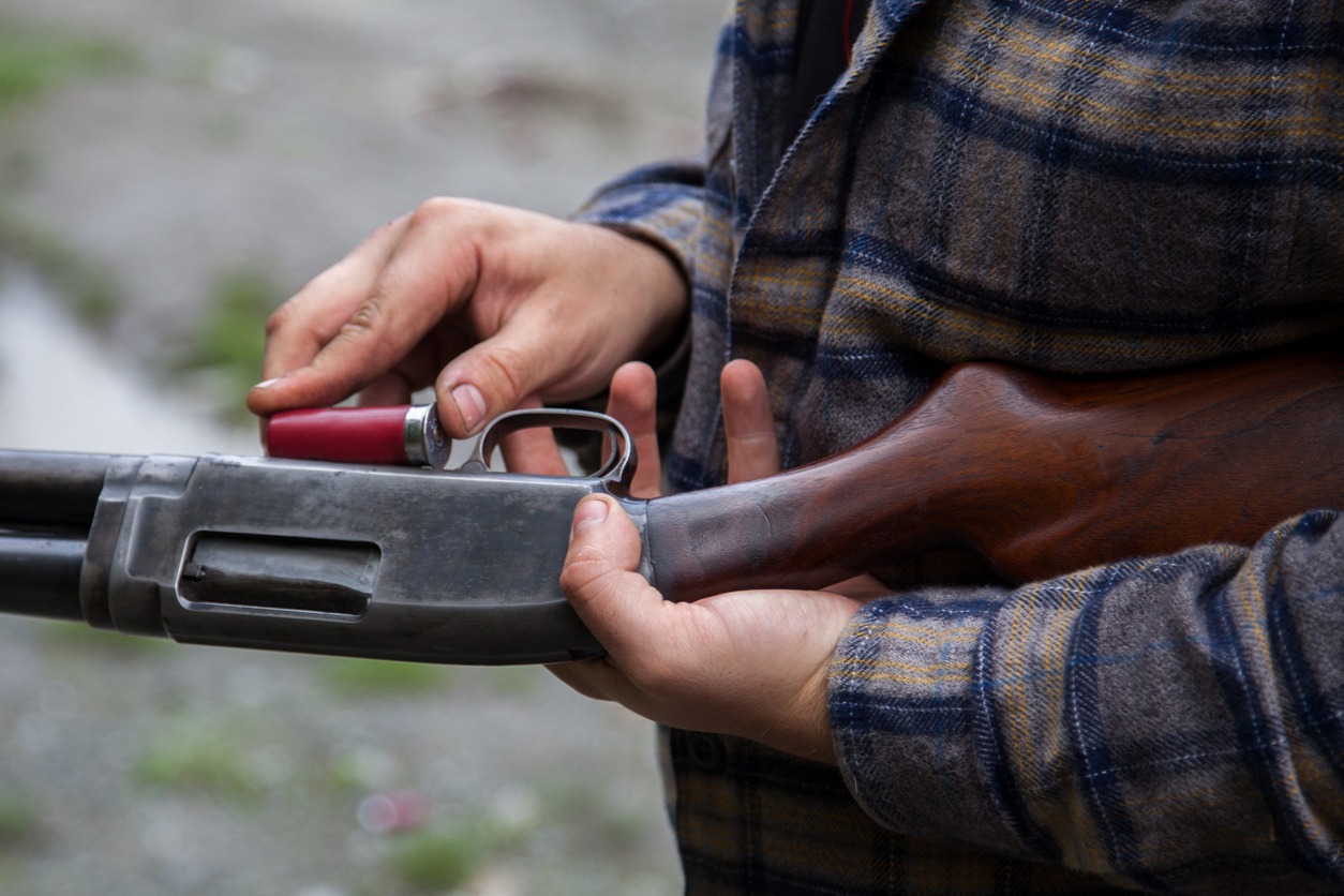 Close up of man loading a red shotgun shell into the magazine of his gun. It has a wooden stock against the steel action
