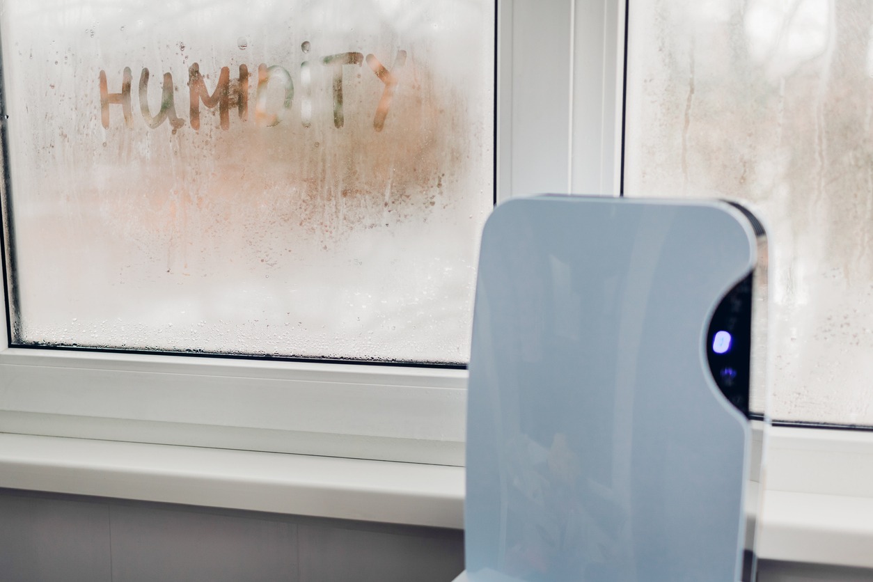 Dehumidifier with touch panel works by wet window in flat. Humidity written on window. High dampness concept.