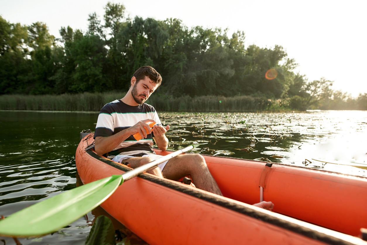 Focused young man applying sunscreen protection while kayaking on the river outdoors